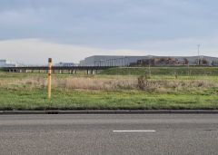 Een lege weg met grasland, een gasuniepaaltje op de voorgrond en een groot gebouw op de achtergrond.